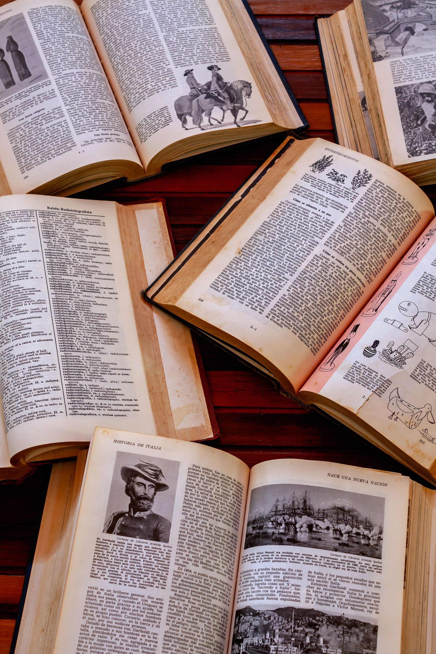 Several vintage books open on a wooden table showcasing illustrations and text.