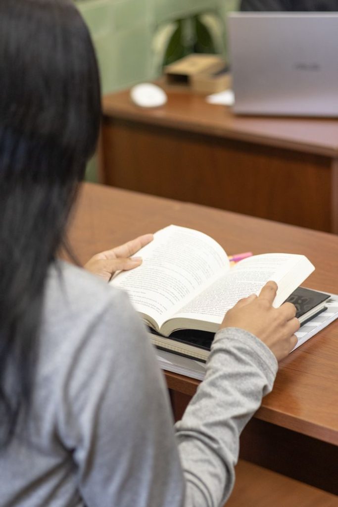 A person reading a book at a desk indoors, capturing a moment of study and concentration.