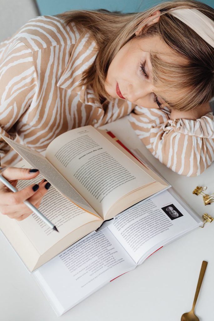 Adult woman studying at a desk with open books and using a pen. Ideal for educational themes.
